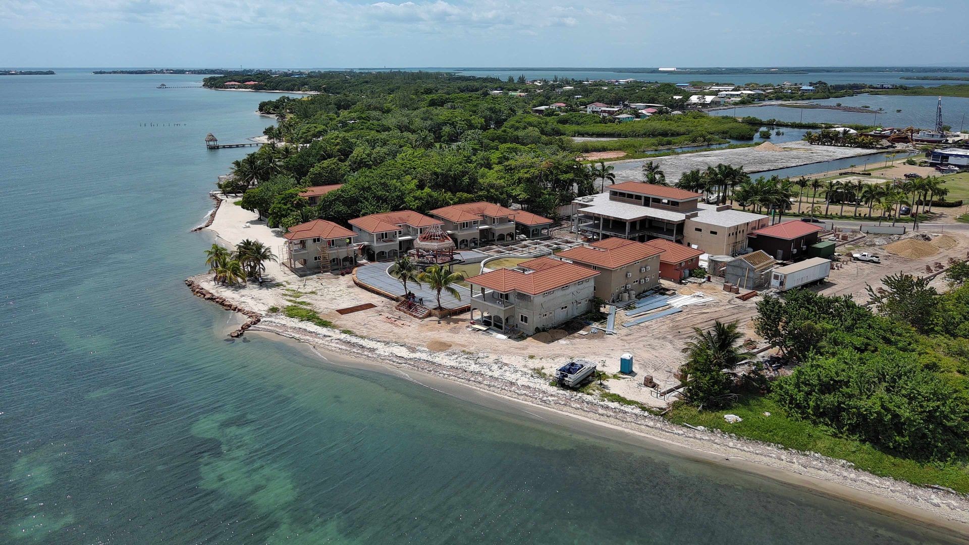 Aerial view of beachfront properties with red roofs, surrounded by lush greenery and ocean.