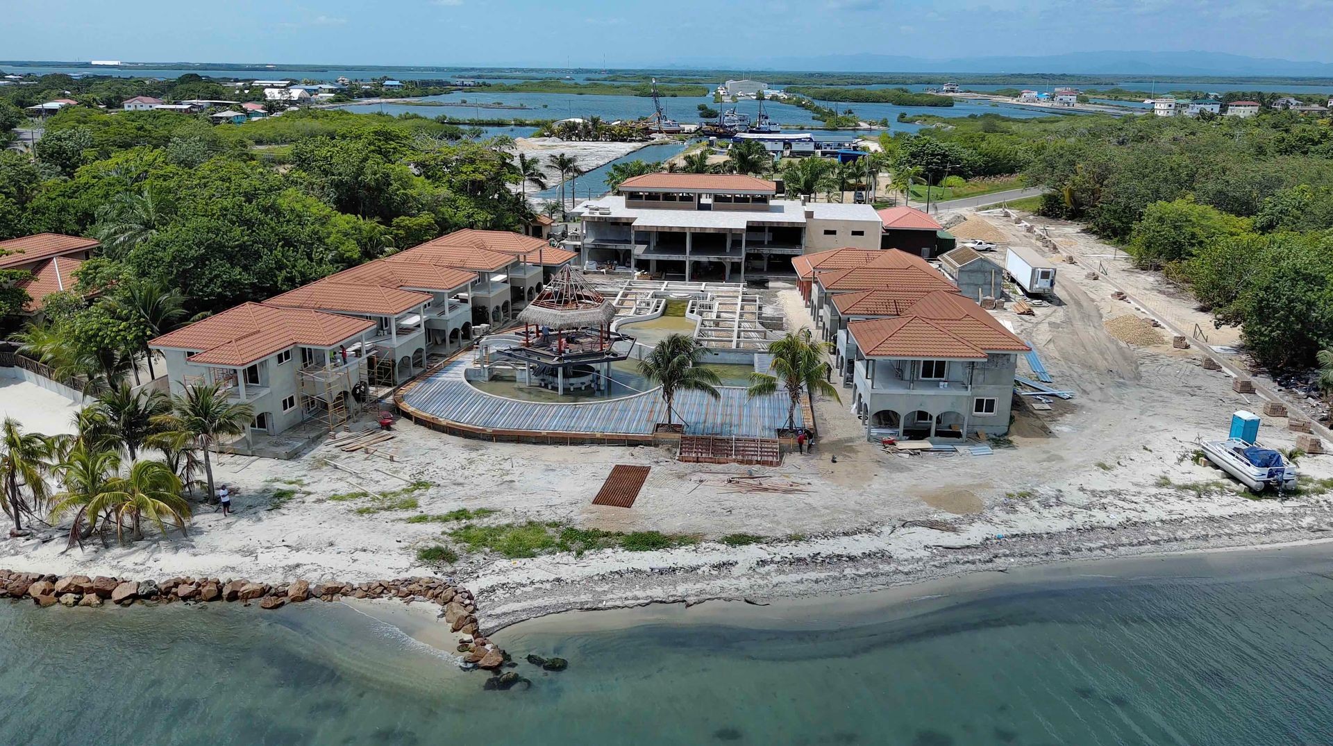 Aerial view of a coastal resort under construction with red-roofed buildings and surrounding greenery.