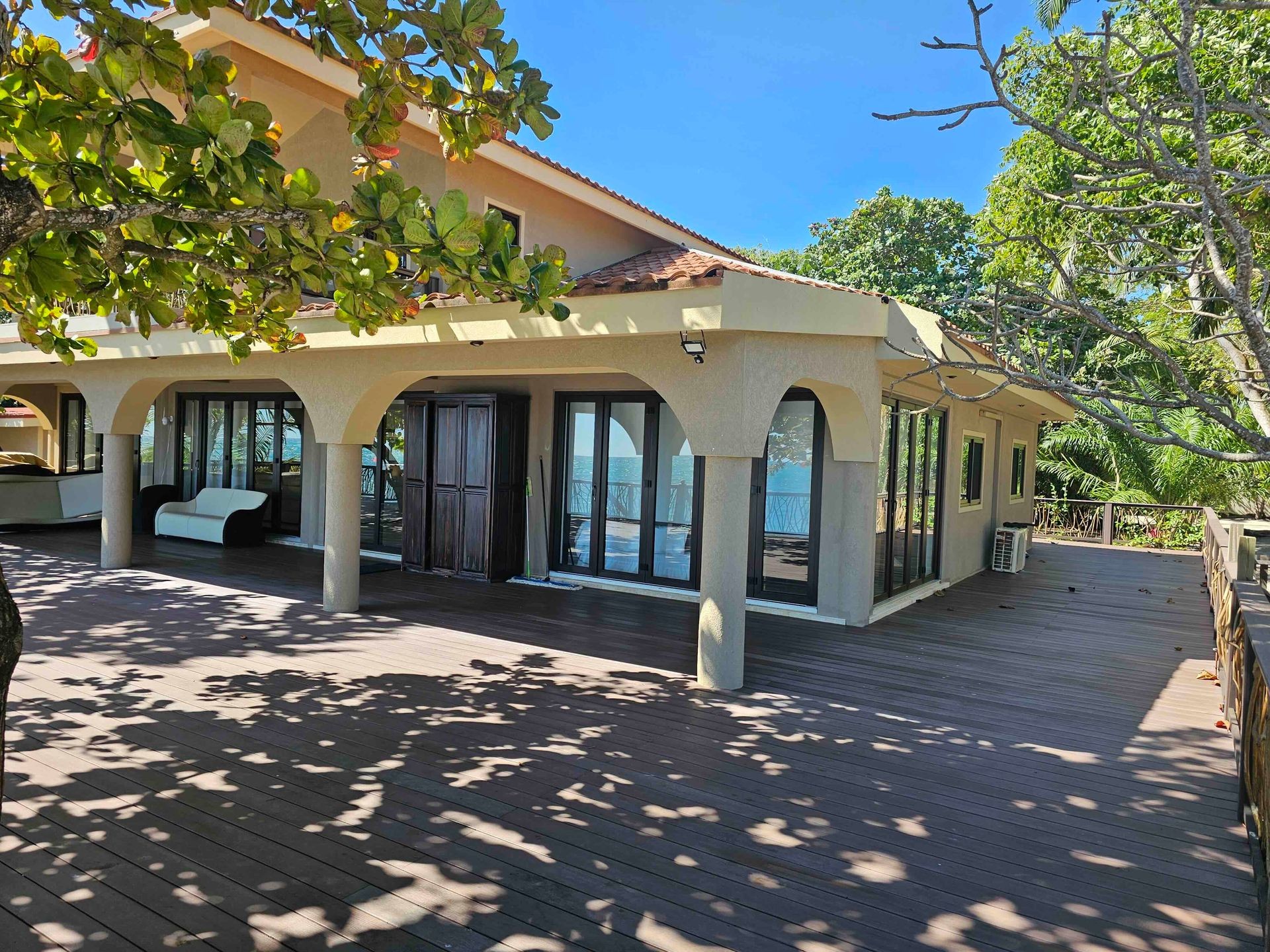 Modern house with large glass doors, surrounded by trees and wooden deck under a clear blue sky.