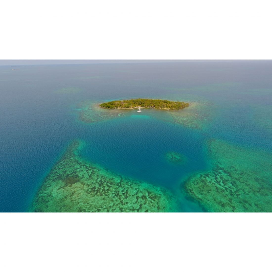 Aerial view of a small island surrounded by clear turquoise water and coral reefs.