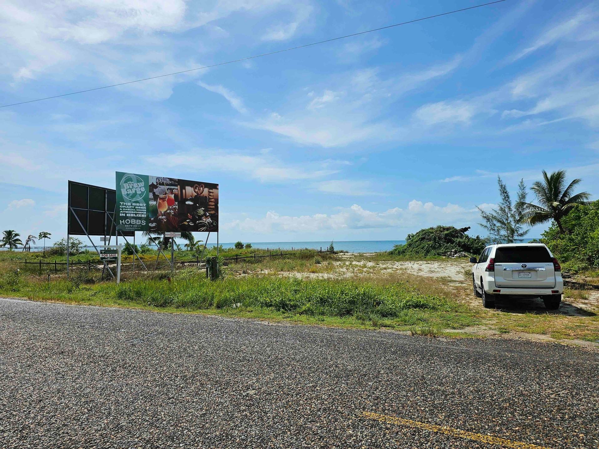 Billboard and white SUV near a beach under a blue sky with clouds.